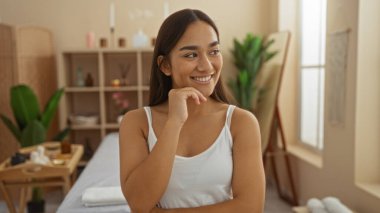 Genç, güzel, esmer, ispanyol, bir sağlık merkezinin içinde gülümseyen sakin ve rahatlatıcı bir ev dekorasyonu olan bir kadın sağlığını, güzelliğini, gençliğini ve sükunetini gösteriyor..