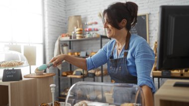 Bir pastanede çalışan bir kadın, içinde maşayla glütensiz hamur işleri servis ediyor..