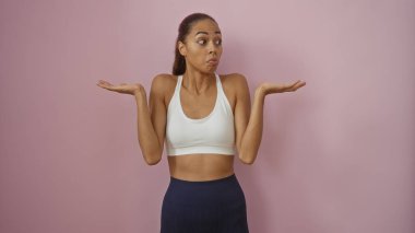 Genç bir kadın atletizm kıyafetlerinde pembe arka plan yüzünden omuz silkiyor..