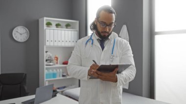 Hastane odasındaki panoya sakallı genç adam modern iç mimari, doktor kıyafeti, beyaz önlük, steteskop, kapalı mekan, odaklanmış ifade, profesyonel çevre..