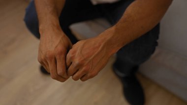 Genç Afro-Amerikalı bir adam ellerini sıkmış bir şekilde oturma odasında oturuyor.