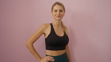 Pembe bir duvara yaslanmış duran genç bir kadın, çağdaş eğilimleri yansıtan sakin ve çekici bir tavırla modern fitness ve gündelik stil sergiliyor..