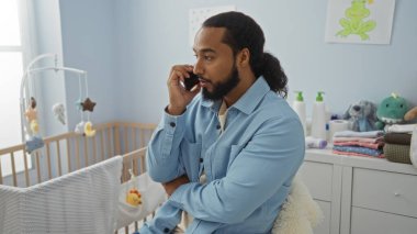 Yatak odasında sakallı genç bir adam bebek beşiğinin yanında konuşuyor. Etrafı yumuşak oyuncaklar ve bebek eşyalarıyla çevrili..