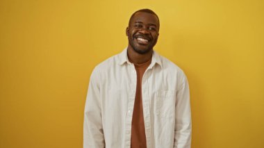 Sarı arka planda duran yakışıklı genç adam neşeyle gülümsüyor.