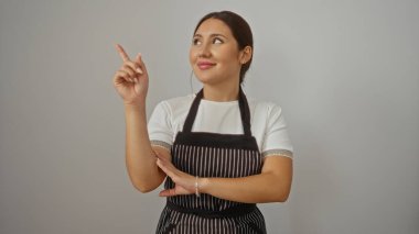 Önlüklü genç bir kadın, izole edilmiş beyaz arka planda parmak uçlarını işaret ediyor..