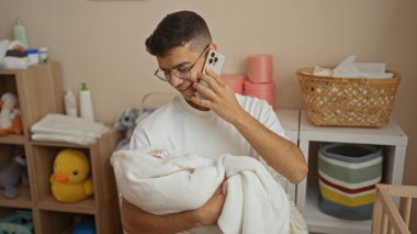 Çocuk odasında telefonla konuşurken kucağında bebeği tutan genç adam hastane odasında sıcaklığını ve bağlantısını iletiyor..