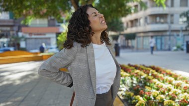 Şehir parkında dikilen bir kadın çiçeklerle ve binalarla çevrili dışarıda huzursuzluk hissediyor. Şehir hayatını ve olgun ifadesini sergiliyor..
