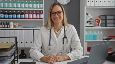 Hastanenin içinde, masasında steteskopla gülümseyen bir kadın sağlık hizmetleri promosyonu için uygun profesyonel ve kendinden emin bir atmosfer sunuyor.