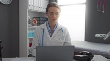 Tıbbi ekipman ve kayıtlarla klinik bir ortamda dizüstü bilgisayarda çalışan kadın doktor modern bir hastane odasında odaklanmış profesyonel bir atmosfer sergiliyor..