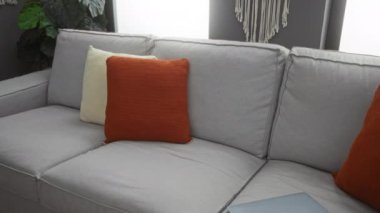 Sakallı genç adam oturma odasında dizüstü bilgisayarla çalışıyor gri kanepe ve turuncu yastıklarla.