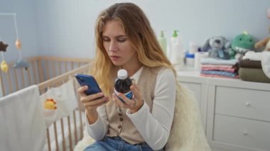 Bebek bakıcılığı yapan kadın akıllı telefonuyla ilaçlarını kontrol ediyor. Etrafı bebek malzemeleriyle çevrili. Parlak ve sakin yatak odası ortamında endişeli görünüyor..