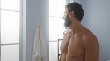 Latin asıllı genç adam, spa merkezinde üstsüz ve büyük pencerelerden içeri ışık giriyor.