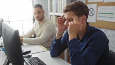 Ofiste çalışan bir adam, mavi gömlekli bir adam stresli, beyaz gömlekli ikinci bir adam, parlak bir odada bilgisayar ve belgelerle çalışan kapalı bir iş yeri.