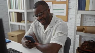 Modern bir ofiste arka planda kitap rafları olan akıllı telefon kullanan yakışıklı bir adam.