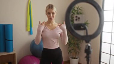 Spor salonunda spor yapan bir kadın, akıllı telefonuyla spor salonunda spor aletleri ve bitkilerle video çekiyor..