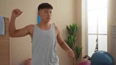 Genç adam sağlık merkezinde egzersiz yapıyor. Kapalı alanda bitki ve spor aletleri var.