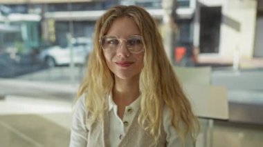 Parlak ofis ortamında gülümseyen, sarı saçlı ve gözlüklü bir kadın modern bir profesyonel atmosfer yaratıyor üretkenlik ve yaratıcılığı gösteriyor..