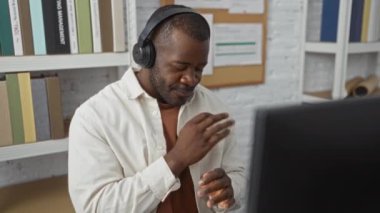 Genç adam, kitaplıklar ve belgelerle çevrili, modern bir çalışma ortamında neşesini ifade eden, mutlu bir şekilde dans ederken, bir ofiste kulaklıkla müzik dinlemekten hoşlanıyor..