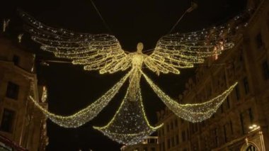 Noel ışıkları Londra 'da bir caddeyi aydınlatıyor. Yukarıda göz kamaştırıcı bir melek süslemesi var. Birleşik Krallık' ta şenlikli bir gece sahnesi yaratıyor..