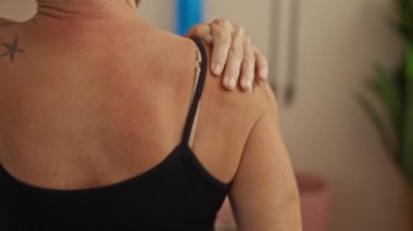 Spor salonunda omuzlarına masaj yapan bir kadın. Sırtında görünür bir dövme var. Rahatlama ve kendine dikkat etme.