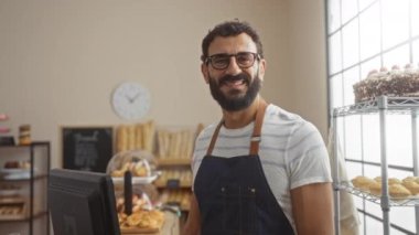 Çizgili gömlekli ve önlüklü İspanyol bir adam fırında pişmiş yiyecekler ve hamur işleriyle gülümsüyor..