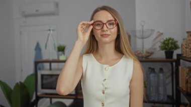 Ofiste kırmızı gözlükler takmış, beyaz bir bluzla gülümseyen bir kadın. Kitaplar ve bitkiler, profesyonel ama rahat bir atmosfer yaratarak iş yeri uyumu öneriyor..