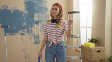 Parlak oturma odasında, merdiven ve tuval kutularıyla yapılan yenileme projesi sırasında modern bir evde resim malzemeleriyle çevrili sıradan kıyafetli bir kadın hayır diyor..