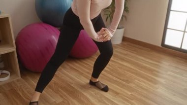 Spor salonunda elleri ve bacakları renkli egzersiz topları ve yumuşak ışıklandırmanın altında ahşap döşeme ile çevrili bir kadın..