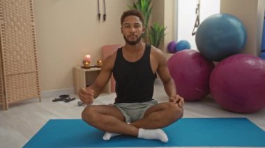 Adam içeride egzersiz yapıyor spor salonunda yoga minderinde geriniyor arka planda fitness topları var odaklanmış bir çalışma ortamı sergiliyor.