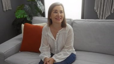 Bir kadın gülümsüyor ve elinde sarı bardakla modern oturma odasında başka bir kadınla.