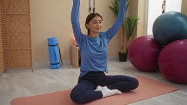 Yoga ekipmanları ve egzersiz toplarıyla çevrili spor salonunda esneyen genç bir kadın, kapalı bir odada mavi giysiler içinde yakalandı..
