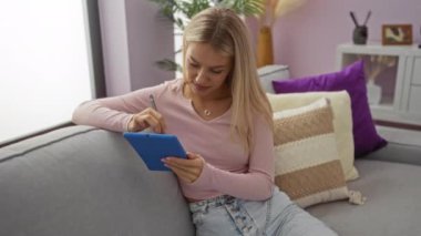 Kadın rahat oturma odasında bitki ve dekoratif yastıklarla tablet kullanıyor, modern ev dekorasyonu ve teknoloji kullanımı sergiliyor.