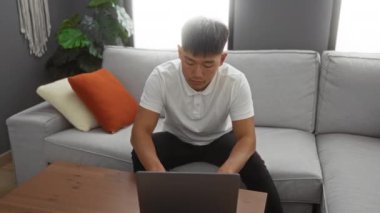 Beyaz gömlekli genç adam, modern apartmandaki kanepeye uzanıyor yastığı tutuyor, rahatlatıyor ve evde derin derin düşünüyor..