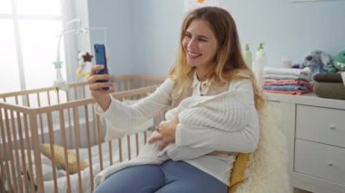 Sıcak yatak odasında bebekle selfie çeken bir kadın beşikte ve neşeli bir atmosferde..
