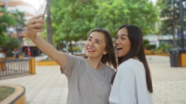 Şehir parkında akıllı telefondan selfie çeken kadınlar doğal şehir ortamında mutluluğu ve kaynaşmayı gösteriyorlar..