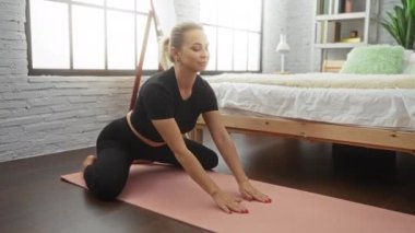 Yatak odasında, rahat yatak odasında, pembe minder üzerinde yoga yapan bir kadın. Ahşap zemin ve sakin ev rahatlığını vurgulayan zarif bir dekor..