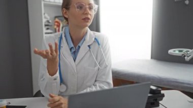 Hastane odasında gözlüklü ve steteskoplu bir kadın doktor laptoptaki video ile hasta danışmanlığını tartışıyor..