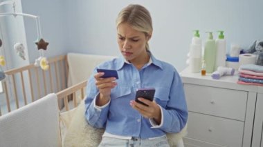 Ev ortamında bebek beşiği olan rahat yatak odasında kredi kartı ve telefonu kontrol eden bir kadın sıcak ve samimi bir atmosfer yaratıyor..