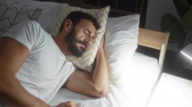 Yumuşak ışıklandırmalı ve rahat yastıklı rahat bir yatak odasında uyuyan yakışıklı bir adam.