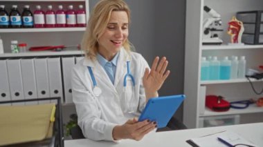 Steteskoplu kadın doktor, klinikte tıbbi araç gereçler ve dokümanlarla modern sağlık hizmetleri iletişimini gösteren video çağrısı yapıyor..