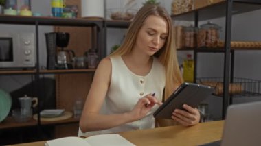 Defterde yazan kadın, modern ofiste tablet kullanırken arka planda raflar meşgul iş yeri ayarlarını gösteriyor.