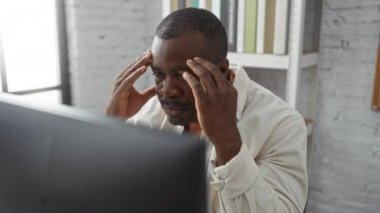 Ofis ortamında stresli bir şekilde çalışan genç bir adam. Baş ağrısı ya da hayal kırıklığını işaret eden elleri şakakların üzerinde.