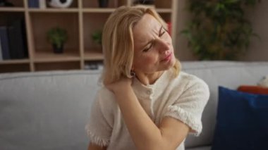 Rahat bir ev ortamında kanepede boyun ağrısı çeken bir kadın modern dekorlu rahat bir oturma odasında olgun bir güzellik ve rahatlama izlenimi uyandırıyor..