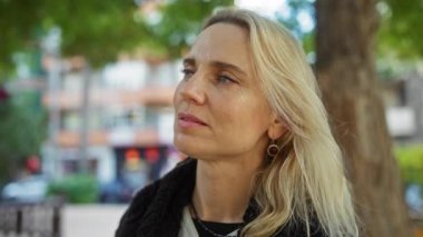 Şehir parkında ağaçlarla gülümseyen ve gün ışığında binaları bulanıklaştıran sakin görünümlü sakin bir şehirde güzellik ve olgunluğu yansıtan bir kadın.