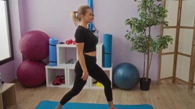 Kadın spor salonunda yoga topu ve ekipmanlarıyla egzersiz yapıyor, siyah spor kıyafetleri giyiyor, ahşap zemini olan açık bir ortamda spor salonuna odaklanıyor..