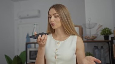 Modern ofis ortamında telefonla konuşan bir kadın, iç dekorlu, sarı saçlı, beyaz bluzlu ve şık arkaplan elementli sıradan ve profesyonel bir çevreyi taşıyor..