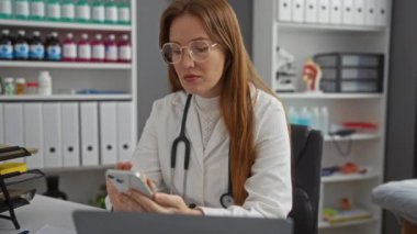 Tıbbi malzeme, dosya ve sağlık ekipmanlarıyla dolu modern bir klinikte steteskopla akıllı telefondan mesaj atan beyaz önlüklü kadın doktor..