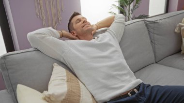 Çağdaş bir apartman dairesinde rahat, gri bir kanepede rahat bir şekilde uzanan yakışıklı genç adam..