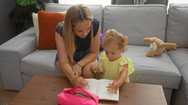 Küçük kızın birlikte oturma odasında pembe bir çantayla tahta masaya çizmesine yardım eden bir kadın.