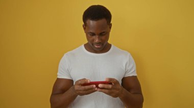 Genç adam canlı sarı arka plana karşı akıllı telefon kullanıyor, modern teknoloji ve dijital bağlantı sergiliyor.